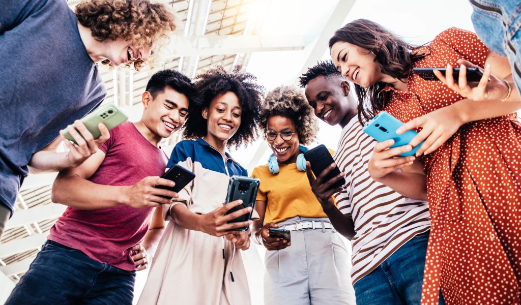 Financial Products That Gen Z Wants A diverse group of Gen Z individuals smiling while using smartphones, emphasizing the need for personalized, mobile-first financial products from credit unions.